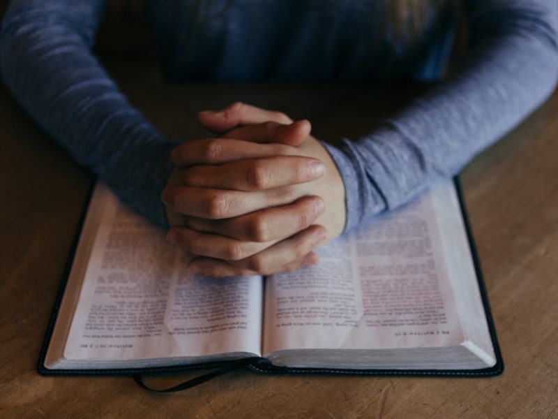 Person folding hands over bible