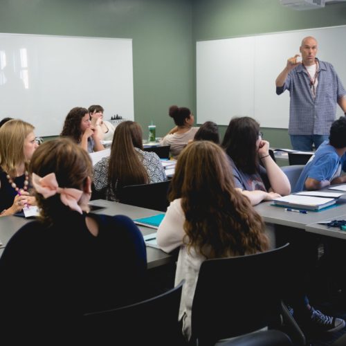 A teacher instructs his class while the studens at their desks follow along